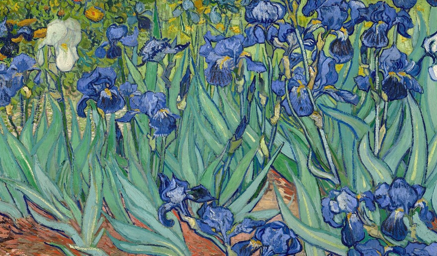A close view of several iris flowers in the painting, showing blue petals built from short, separate brushstrokes against green leaves.